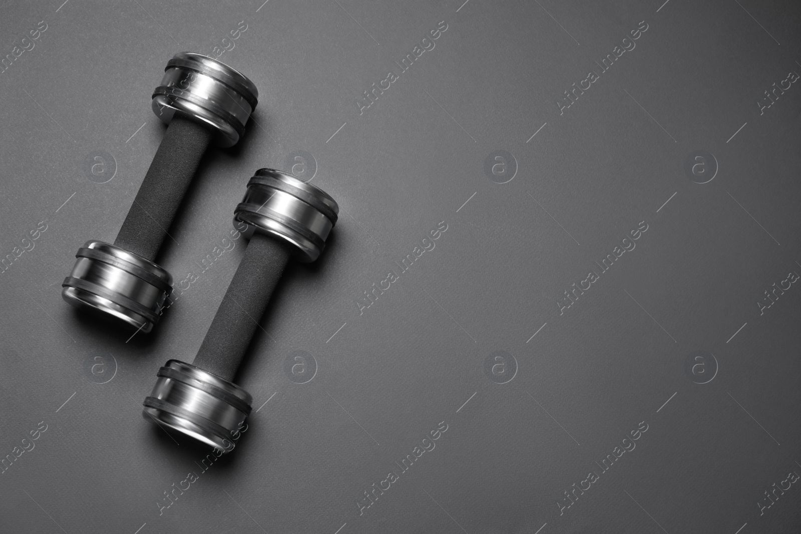 Photo of Metal dumbbells on black background, flat lay. Space for text