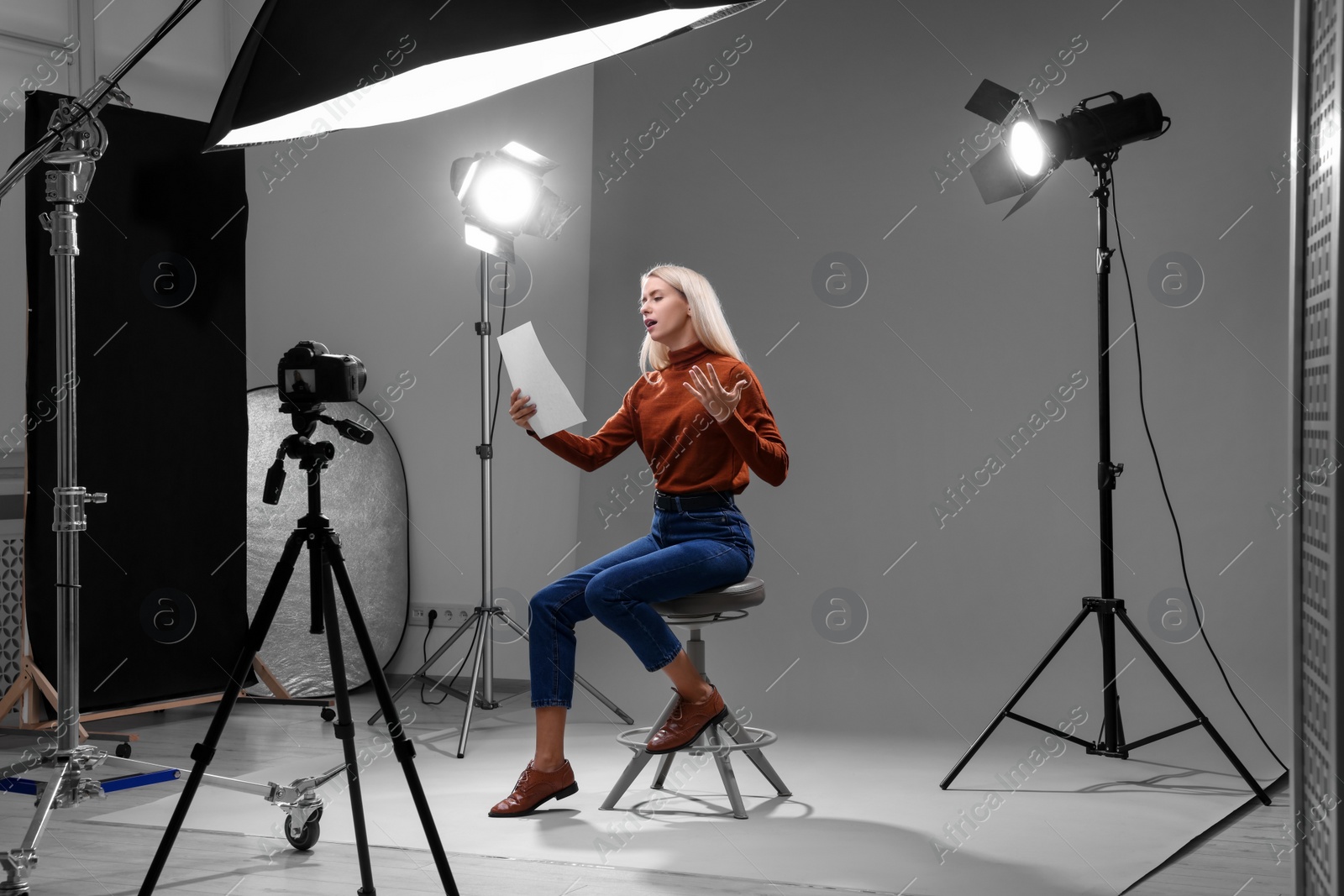 Photo of Casting call. Emotional woman with script sitting on chair and performing in front of camera in studio