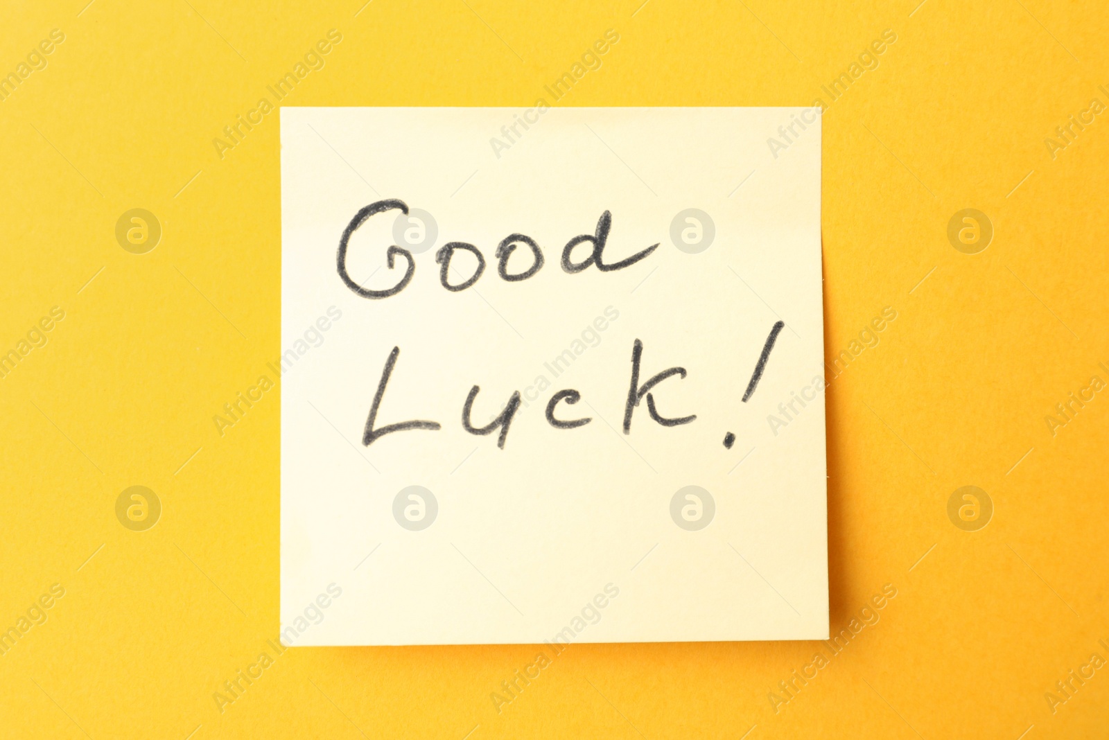 Photo of Note with phrase GOOD LUCK on orange background, top view