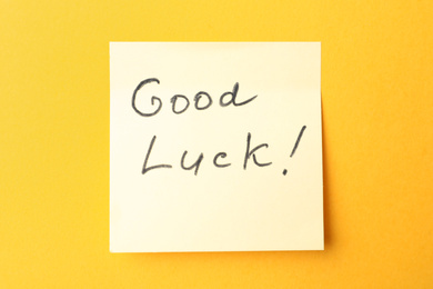 Photo of Note with phrase GOOD LUCK on orange background, top view