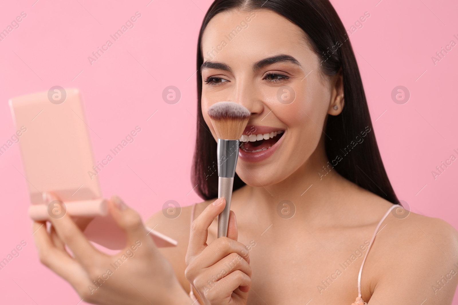 Photo of Beautiful woman with cosmetic pocket mirror applying makeup on pink background