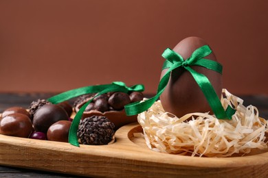 Photo of Tasty chocolate egg with green bow and sweets on wooden board