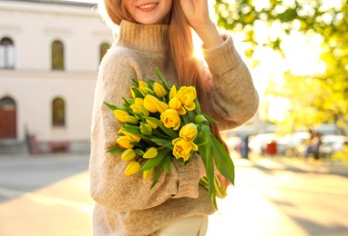 Photo of Teenage girl with bouquet of yellow tulips on city street, closeup