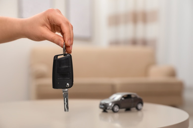 Photo of Man holding key near table with miniature automobile model indoors, closeup. Car buying