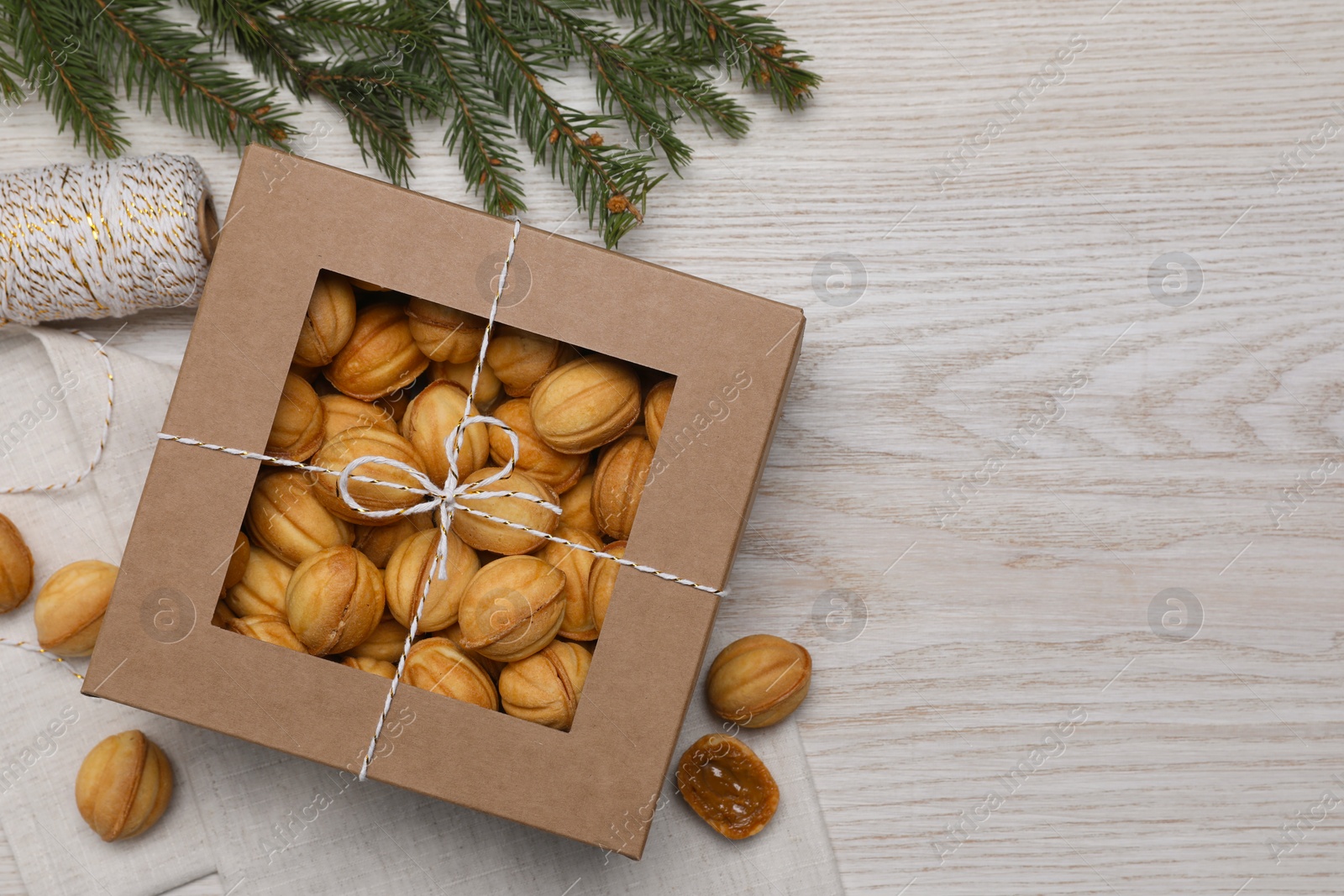 Photo of Delicious nut shaped cookies with boiled condensed milk in box and fir branch on white wooden table, flat lay. Space for text