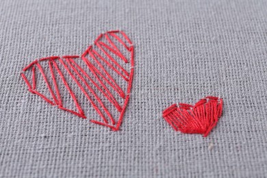Photo of Embroidered red hearts on light grey cloth, closeup