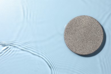 Photo of Presentation of product. Stone podium in water on light blue background, top view. Space for text