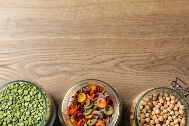 Photo of Glass jars with different products on wooden table, flat lay. Space for text