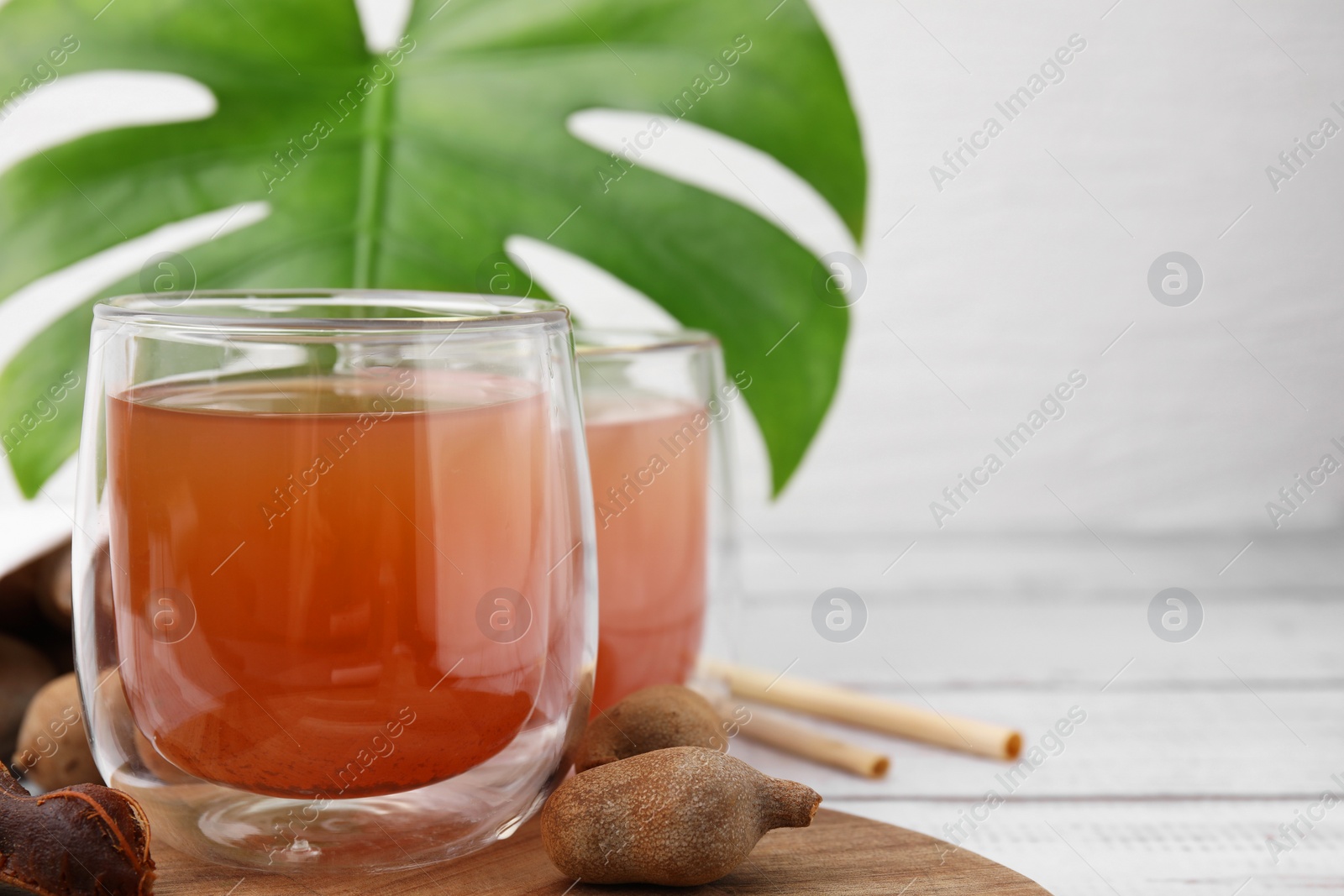 Photo of Tamarind juice and fresh fruits on white wooden table, closeup. Space for text