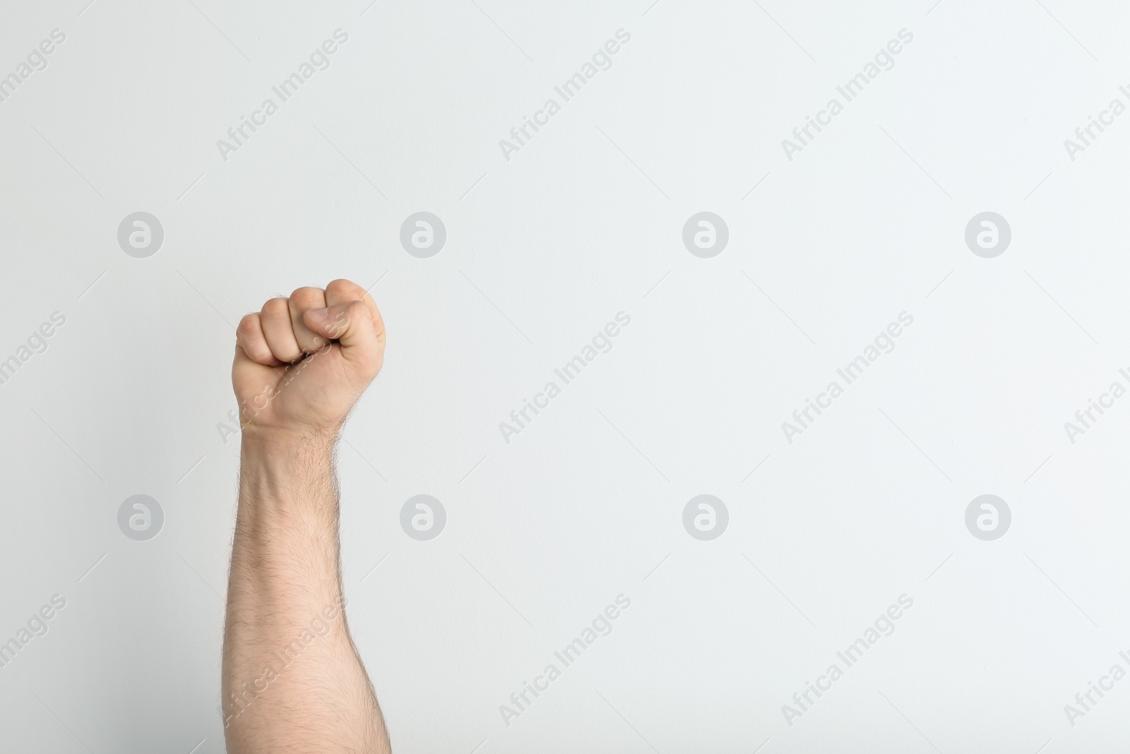 Photo of Young man showing clenched fist on light background. Space for text