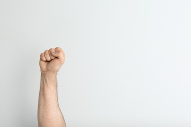 Photo of Young man showing clenched fist on light background. Space for text