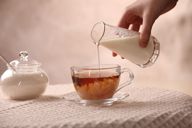 Photo of Woman pouring milk into cup with aromatic tea at table, closeup