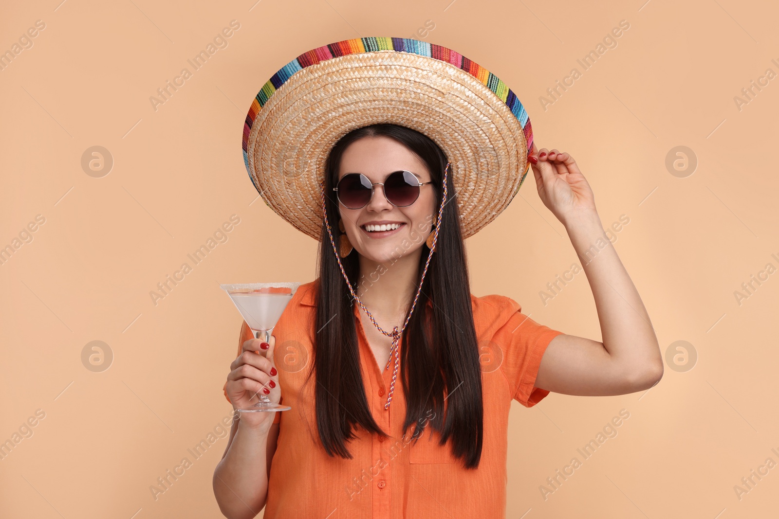 Photo of Young woman in Mexican sombrero hat with cocktail on beige background