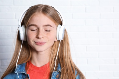 Photo of Teen girl listening to music with headphones near brick wall. Space for text