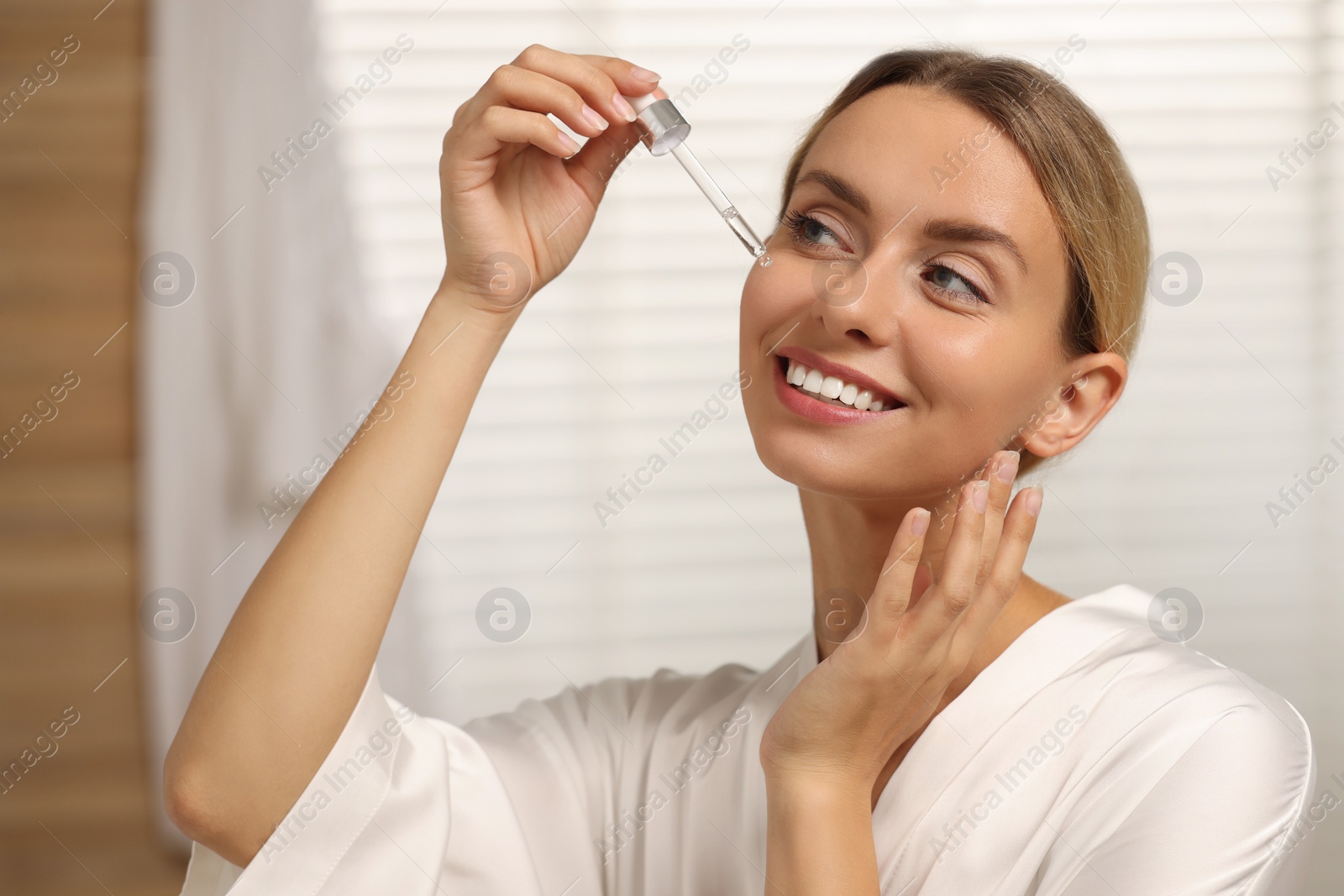 Photo of Beautiful woman applying cosmetic serum onto her face in bathroom