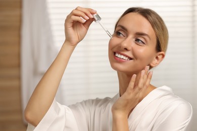 Beautiful woman applying cosmetic serum onto her face in bathroom