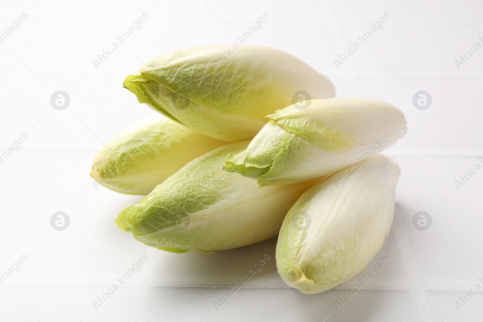 Photo of Fresh raw Belgian endives (chicory) on white tiled table