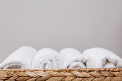 Photo of Set of clean white towels in wicker basket against grey background, closeup with space for text. Tidying up method