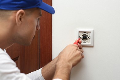 Photo of Professional electrician with screwdriver repairing light switch indoors, closeup