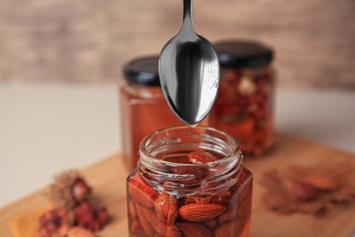 Photo of Honey dripping from spoon into glass jar with nuts, closeup