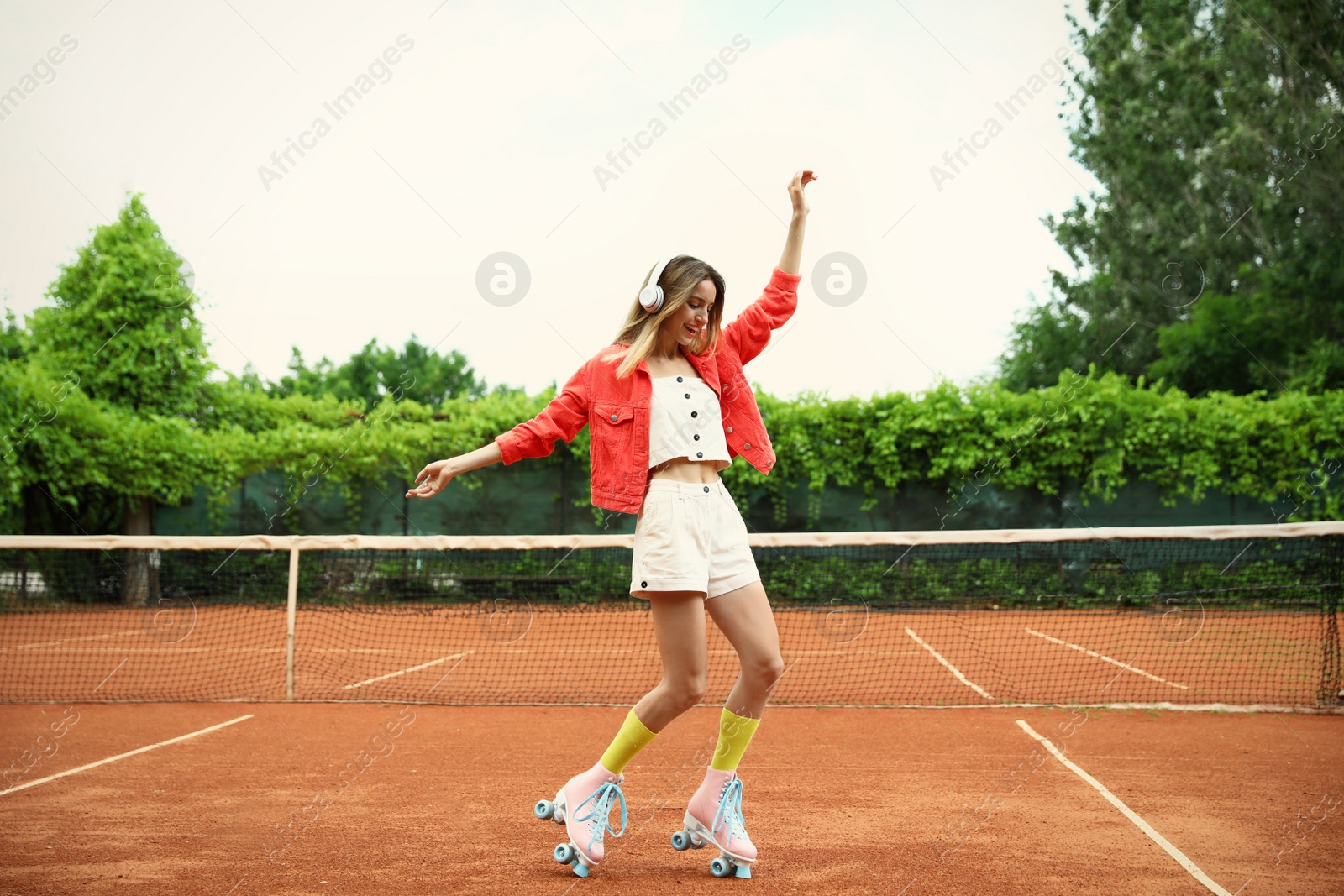 Photo of Happy stylish young woman with vintage roller skates and headphones on tennis court