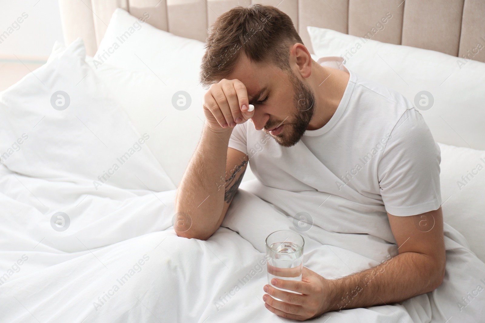 Photo of Man with glass of water and pill suffering from migraine in bed
