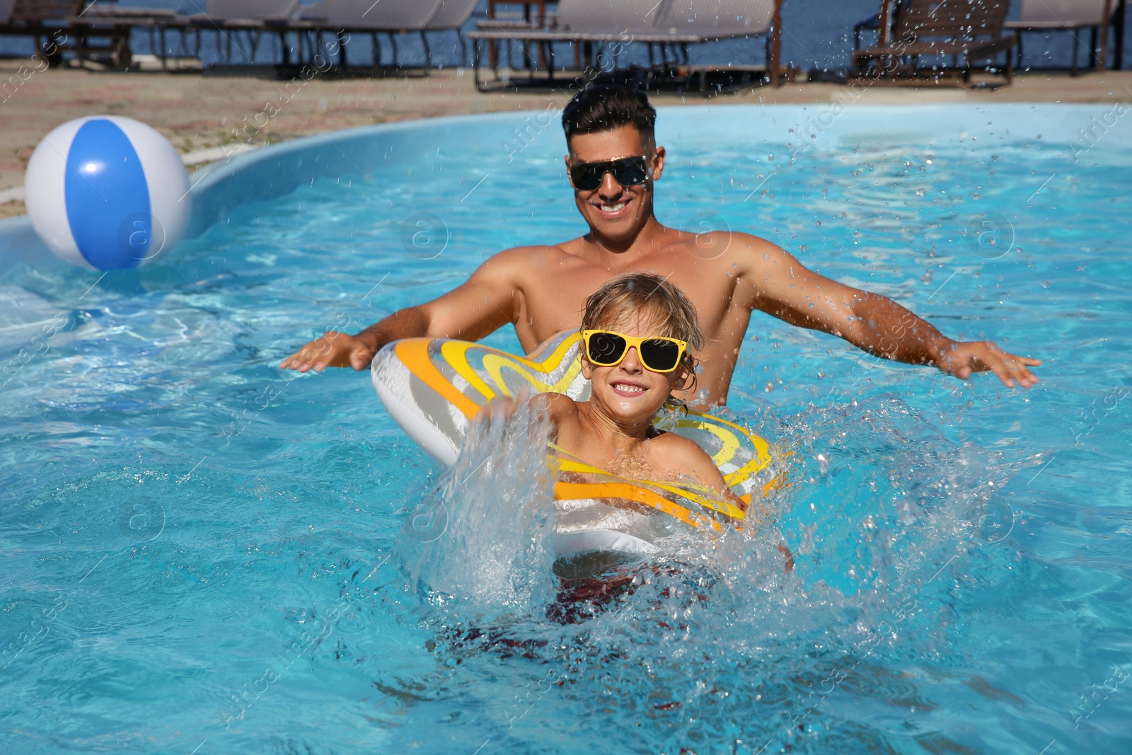 Photo of Happy man and his son with inflatable ring in outdoor swimming pool on sunny summer day