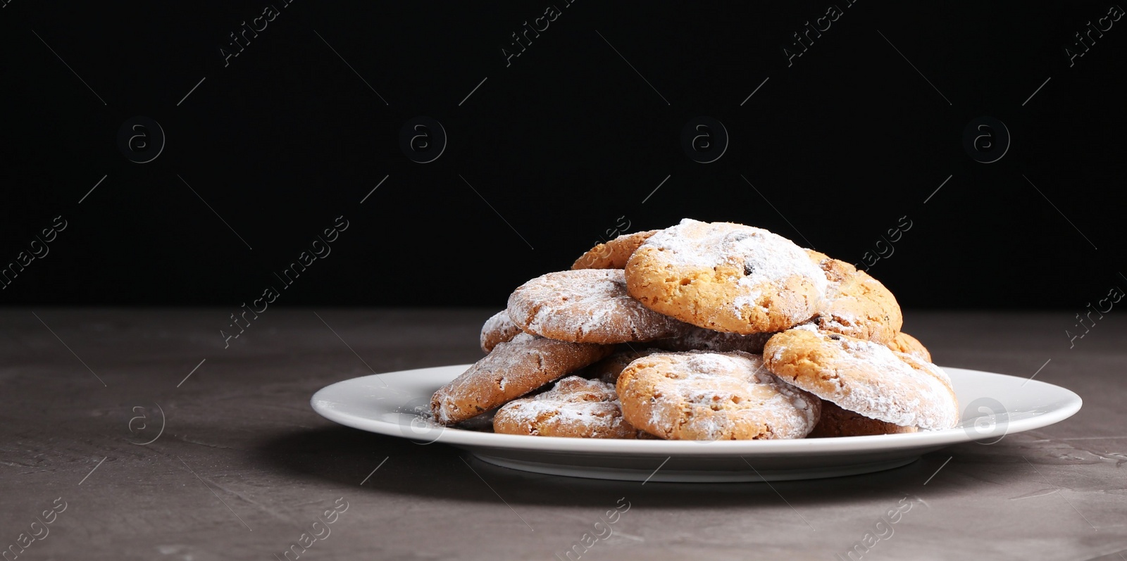 Photo of Woman with sieve sprinkling powdered sugar onto cookies at grey textured table, closeup