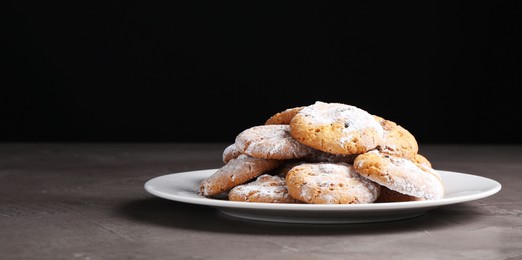 Woman with sieve sprinkling powdered sugar onto cookies at grey textured table, closeup