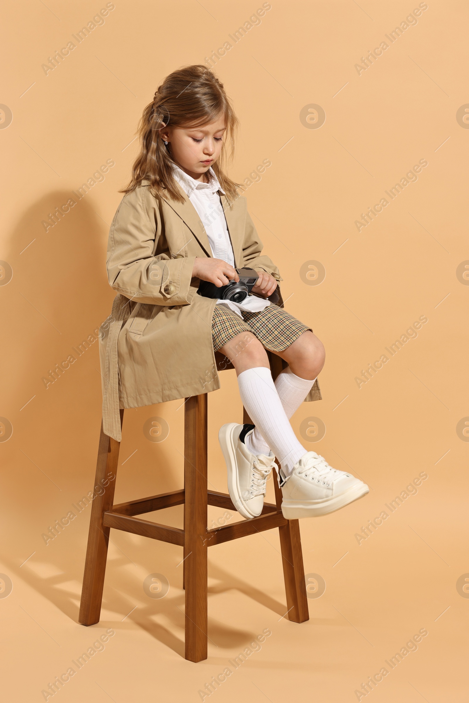 Photo of Fashion concept. Stylish girl with vintage camera on pale orange background