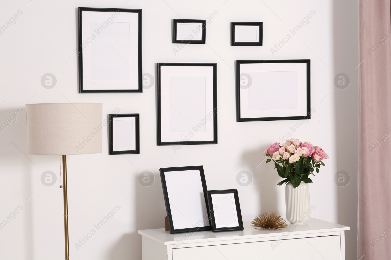 Photo of Empty frames hanging on white wall and chest of drawers with flowers indoors