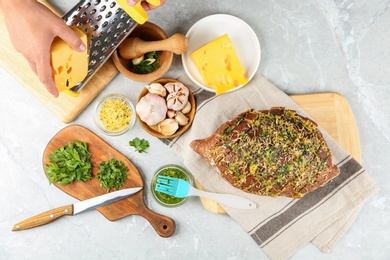 Photo of Woman grating cheese for homemade garlic bread at light table, top view