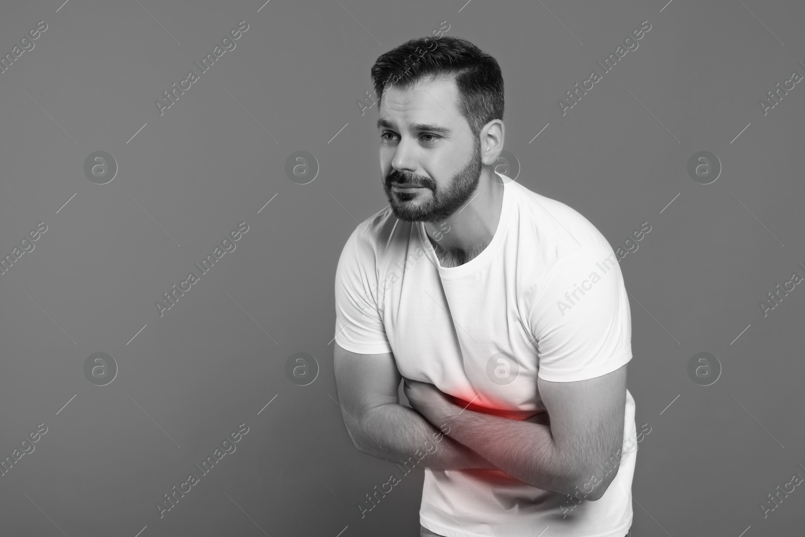 Image of Man suffering from abdominal pain on grey background. Black and white effect with red accent