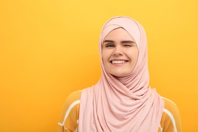 Muslim woman in hijab winking on orange background, space for text