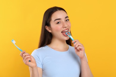 Happy woman brushing her tongue with cleaner and holding plastic toothbrush on yellow background