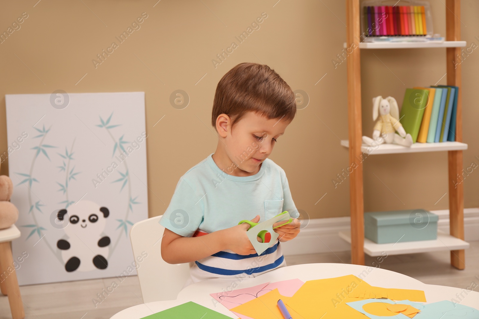 Photo of Little boy cutting color paper with scissors at table indoors