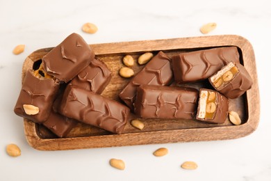 Photo of Wooden board of chocolate bars with caramel, nuts and nougat on white marble table, top view