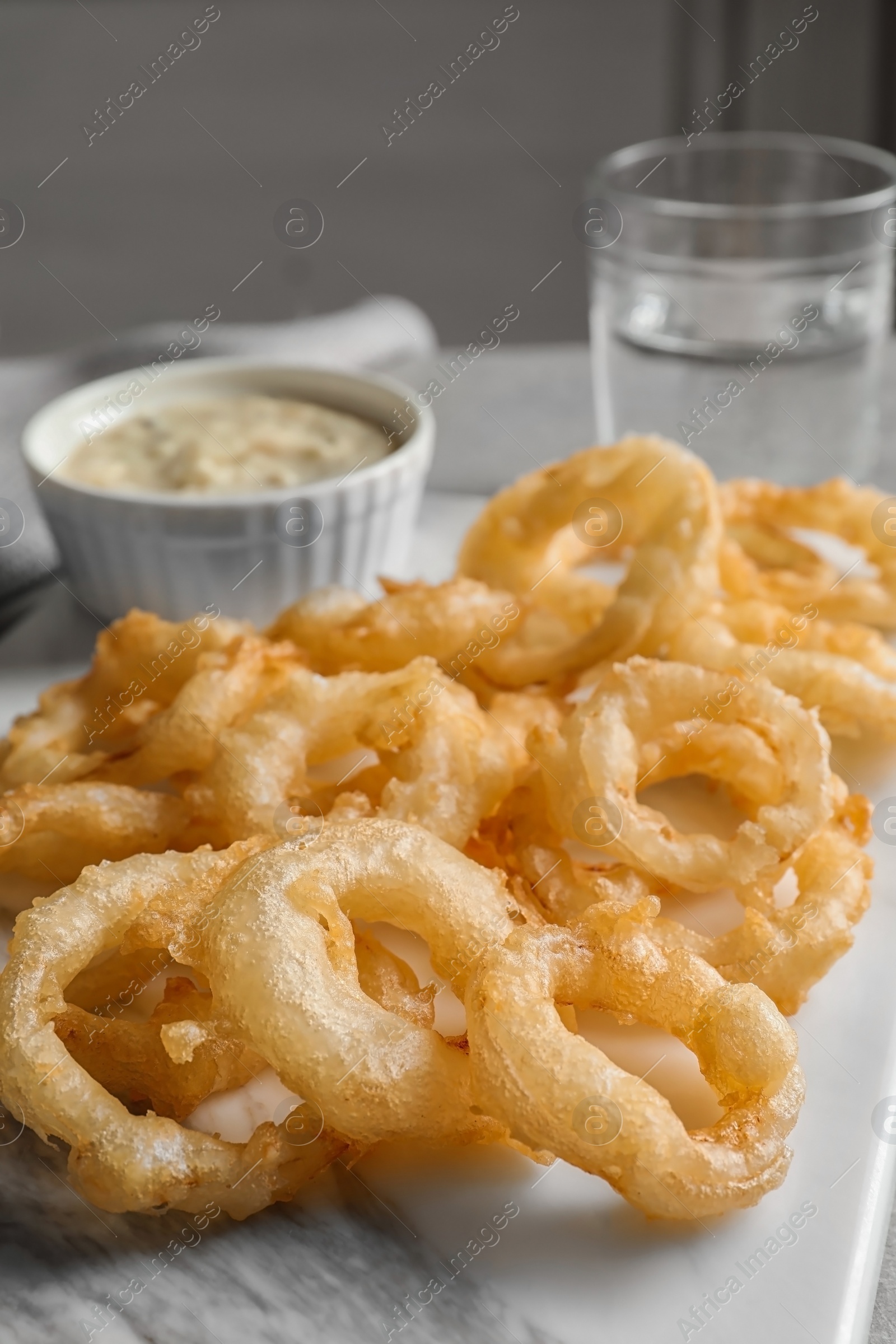 Photo of Closeup view of delicious golden breaded and deep fried crispy onion rings on marble board