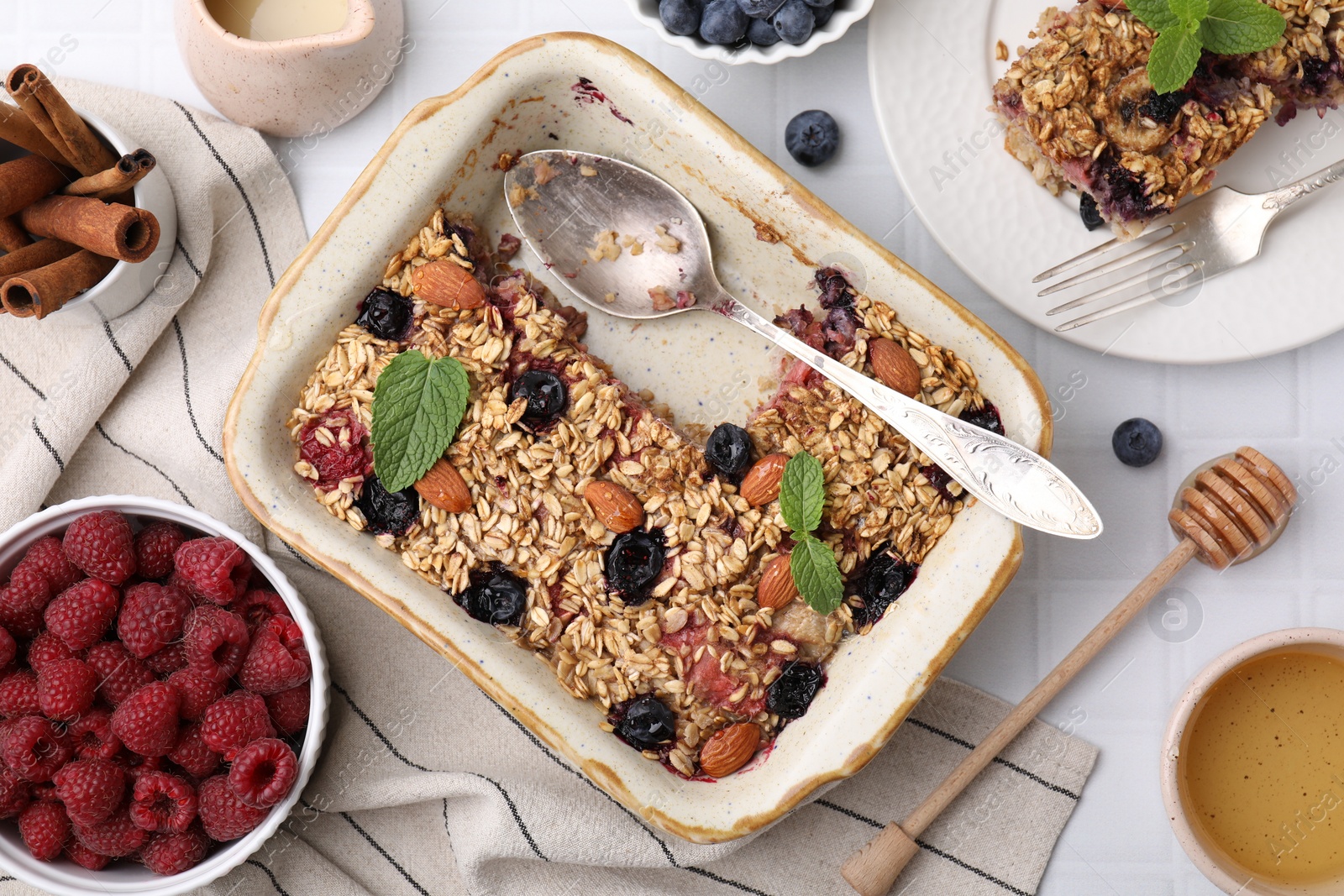 Photo of Tasty baked oatmeal with berries and almonds on white tiled table, flat lay