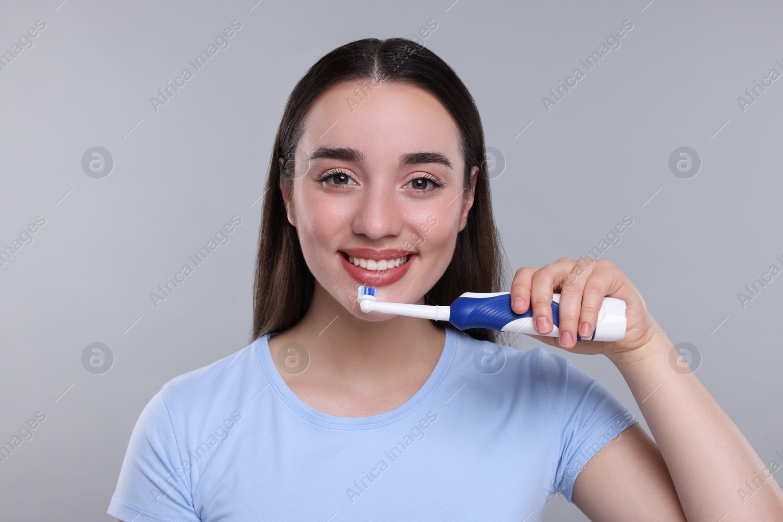 Photo of Happy young woman holding electric toothbrush on light grey background