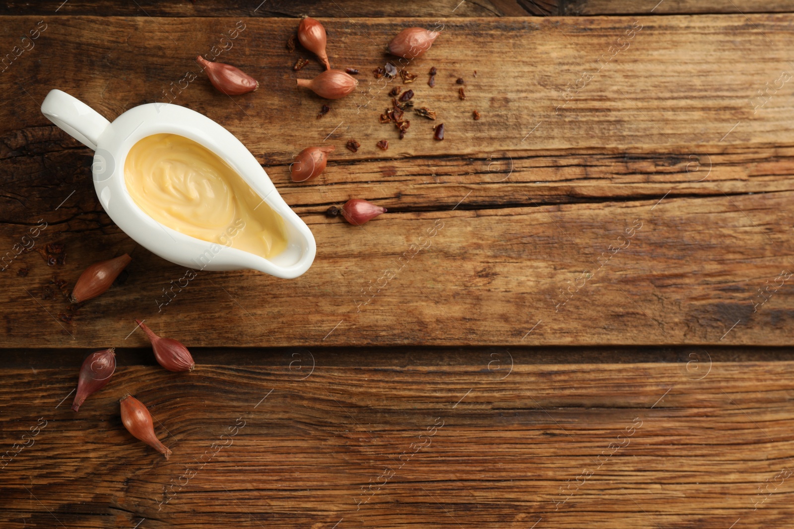 Photo of Tasty sauce in gravy boat, small onion bulbs and spice on wooden table, flat lay. Space for text