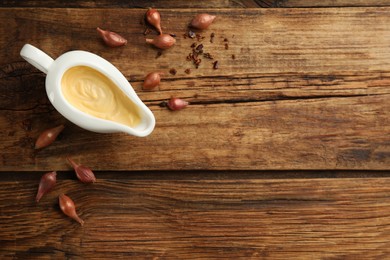 Tasty sauce in gravy boat, small onion bulbs and spice on wooden table, flat lay. Space for text