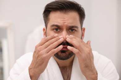 Photo of Skin problem. Confused man touching his face indoors