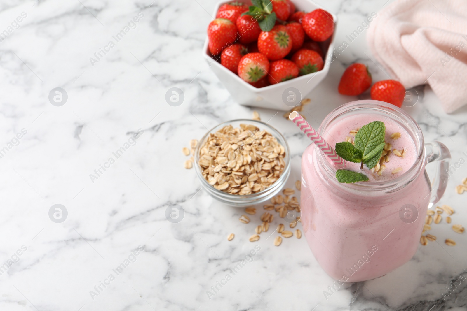 Photo of Mason jar of tasty strawberry smoothie with oatmeal and mint on white marble table, space for text