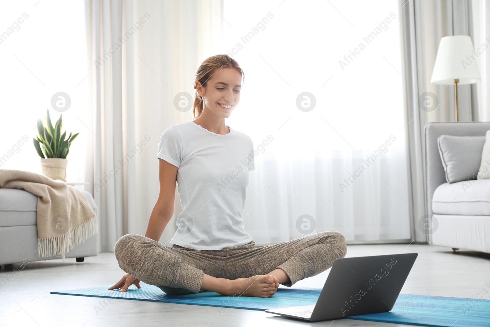 Photo of Woman having online video class via laptop at home. Distance yoga course during coronavirus pandemic