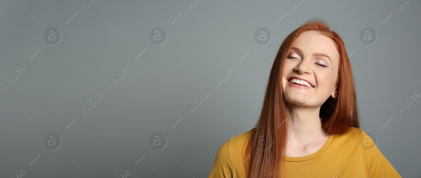 Photo of Candid portrait of happy young woman with charming smile and gorgeous red hair on grey background