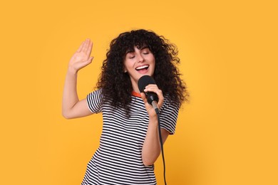 Beautiful young woman with microphone singing on yellow background