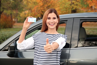 Happy woman holding driving license near car