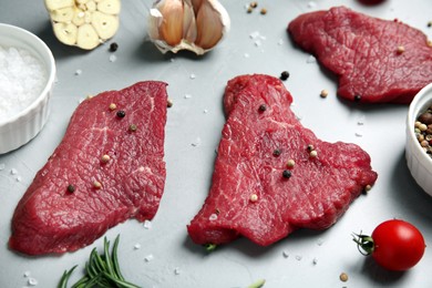 Photo of Fresh raw meat steaks and spices on light grey table