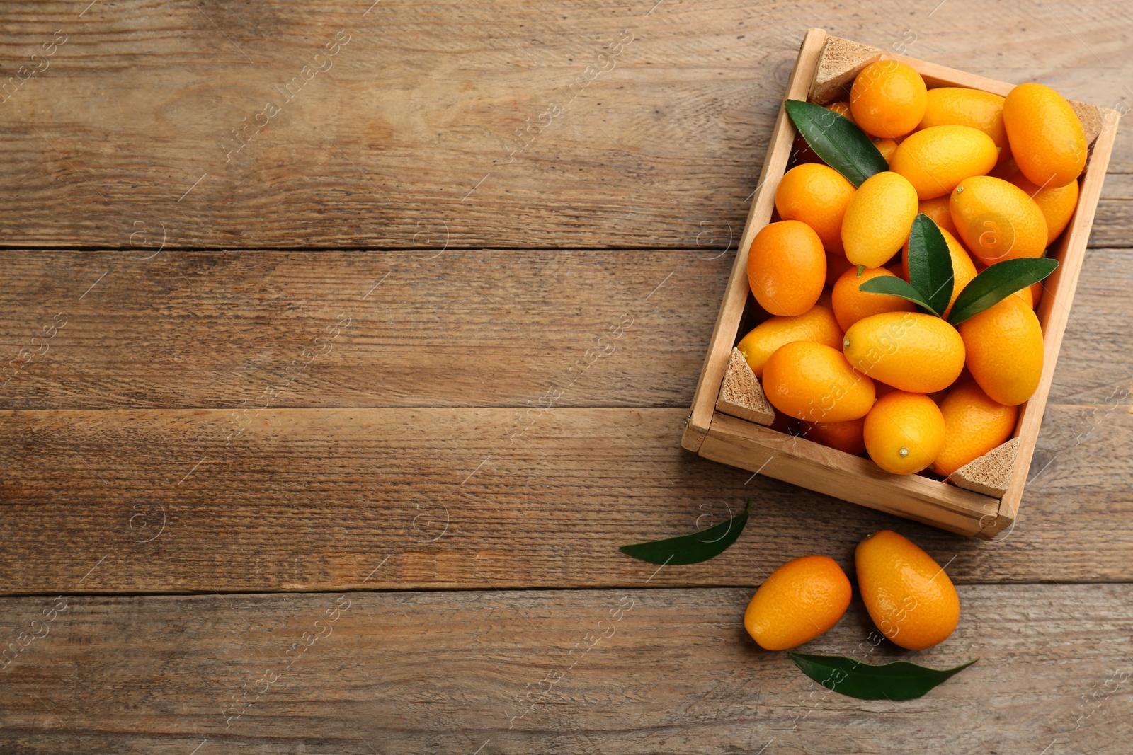 Photo of Fresh ripe kumquats in crate on wooden table, flat lay. Space for text